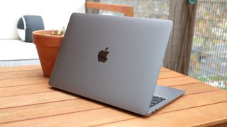 MacBook Air (M1, 2020) on an outdoor wooden coffee table facing away from you showing the logo on the lid