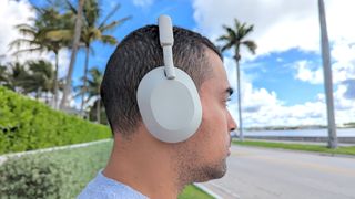 Man Sony WH-1000XM5 wireless headphones outside with blue skies and palm trees in the background
